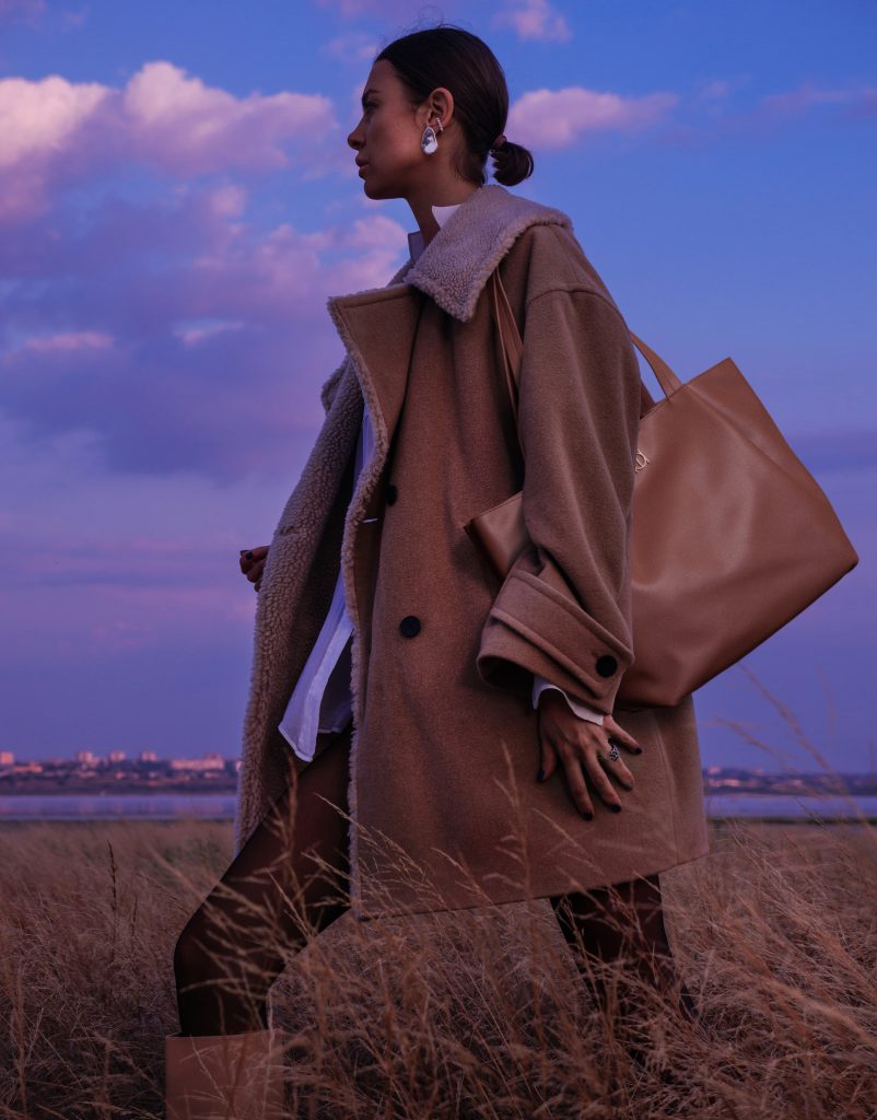 A women with a brown overcoat with sheep's wool carrying a top trending riona vegan fall handbag called Serena from Riona.